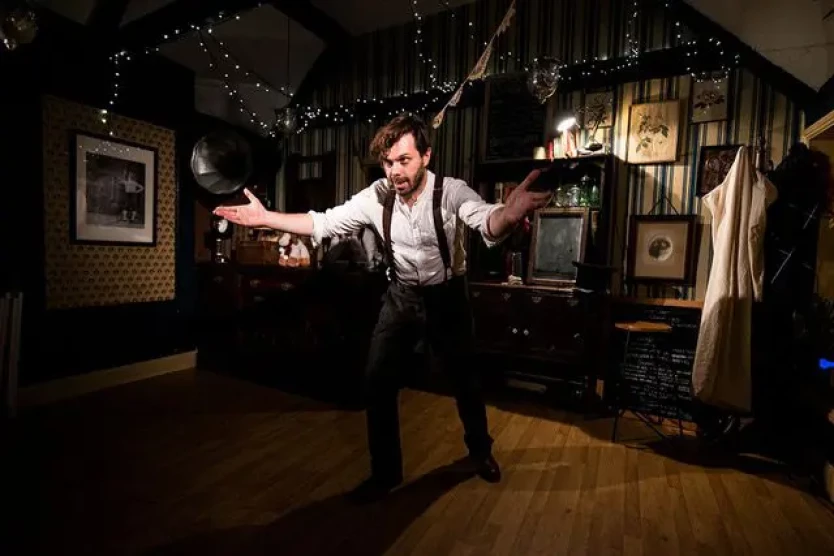 A man gestures towards you, in a Victorian living room set